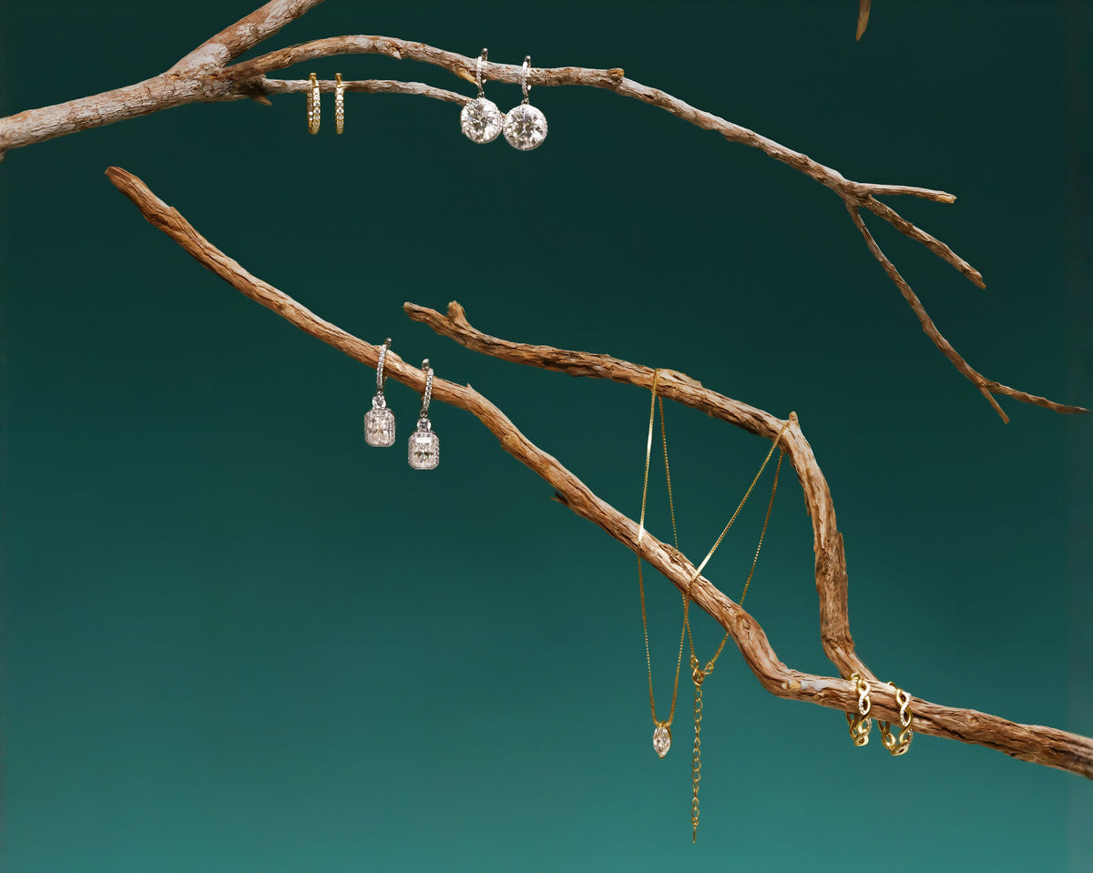 Diamond earrings and delicate gold necklaces displayed on natural wooden branches