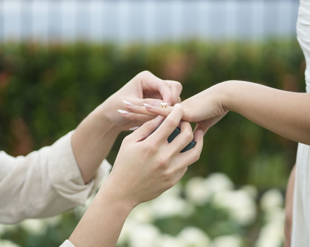 Romantic proposal featuring a marquise solitaire engagement ring being placed on a finger during an outdoor engagement.