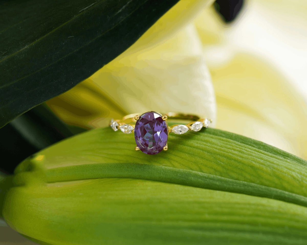 Oval purple gemstone ring with diamond side stones on a yellow gold band