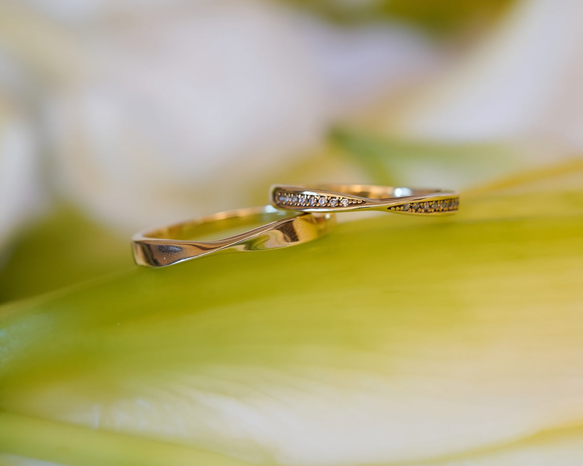 Gold wedding bands with delicate diamond accents displayed on a green leaf