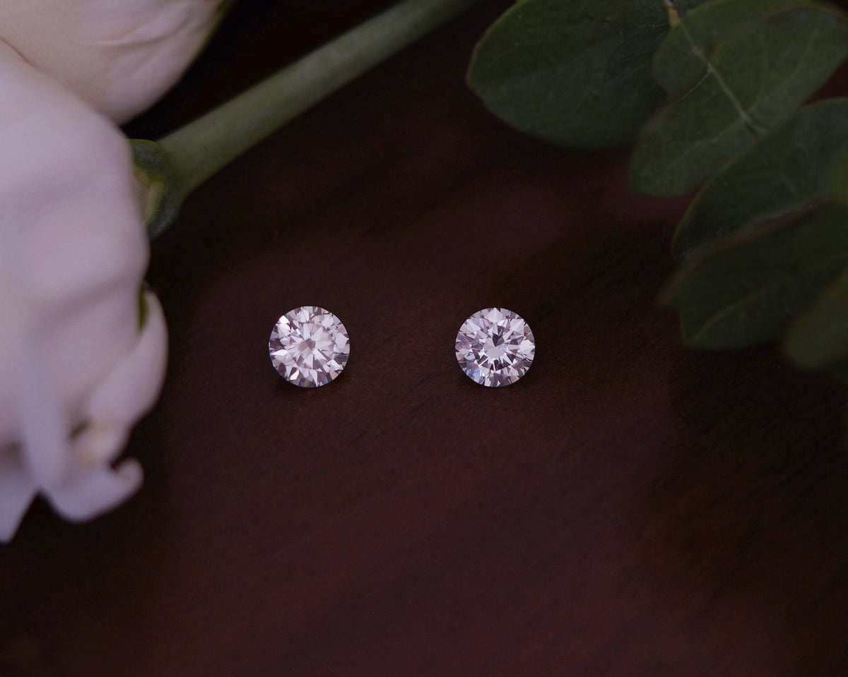 Pair of round brilliant lab-grown diamonds displayed on a wooden surface, ideal for custom engagement rings and fine jewelry.