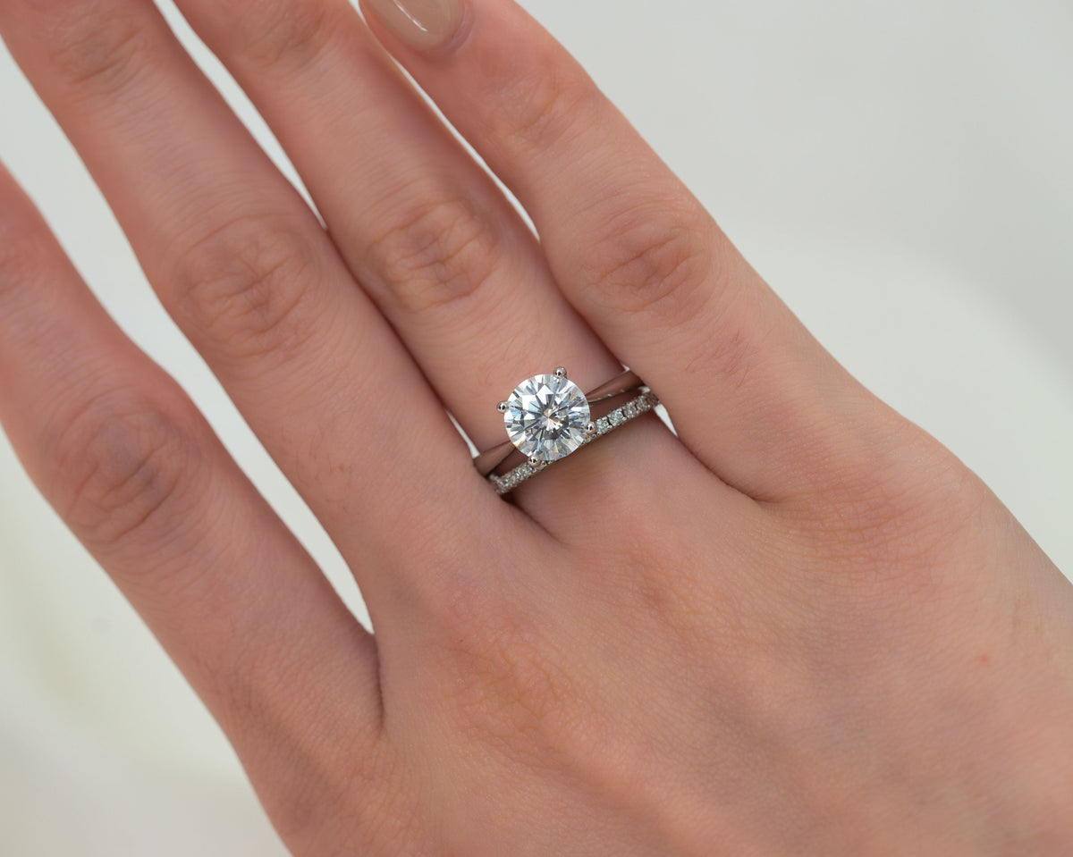 Close-up of a round brilliant solitaire diamond engagement ring in a white gold setting paired with a pavé diamond wedding band on a woman's hand.