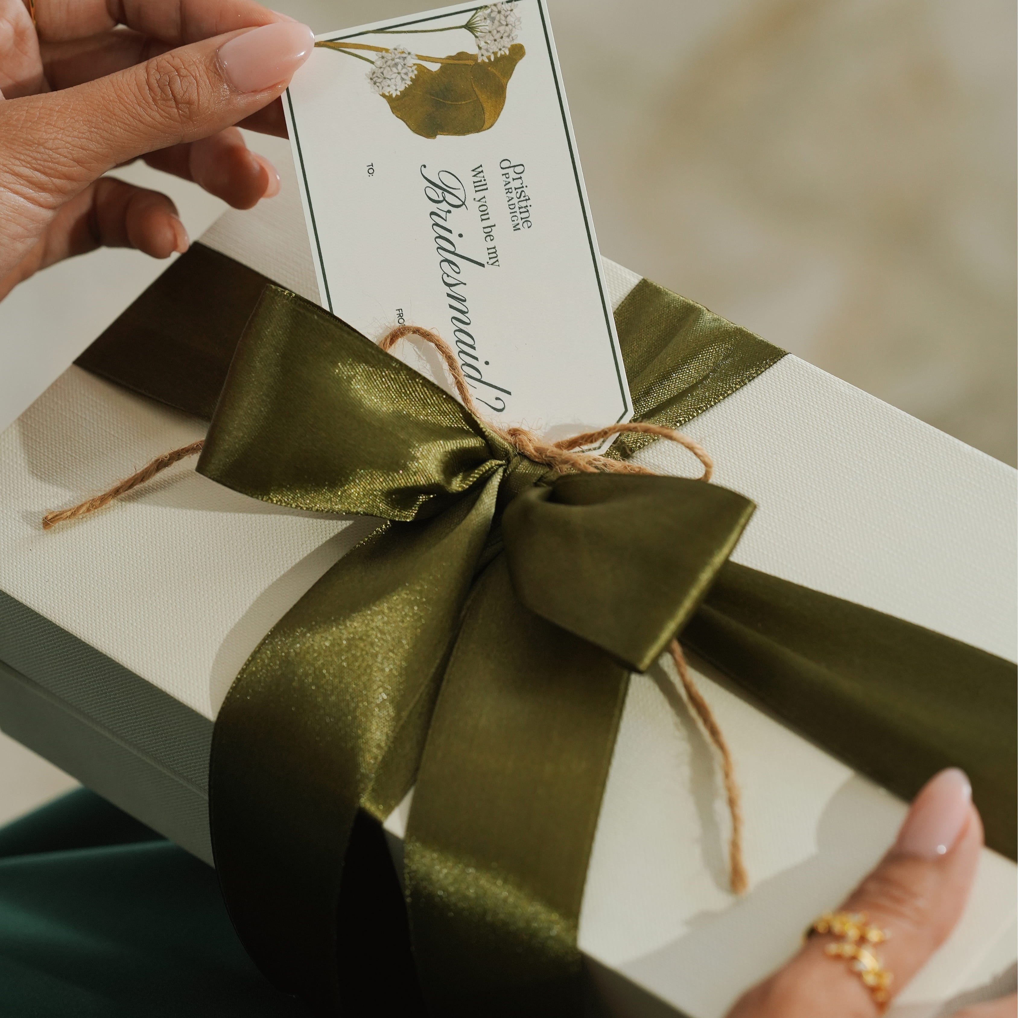 Gift box with green ribbon and card held by hands